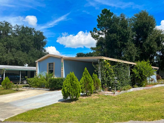 Home with driveway, several plants and bushes, and grassy lawn